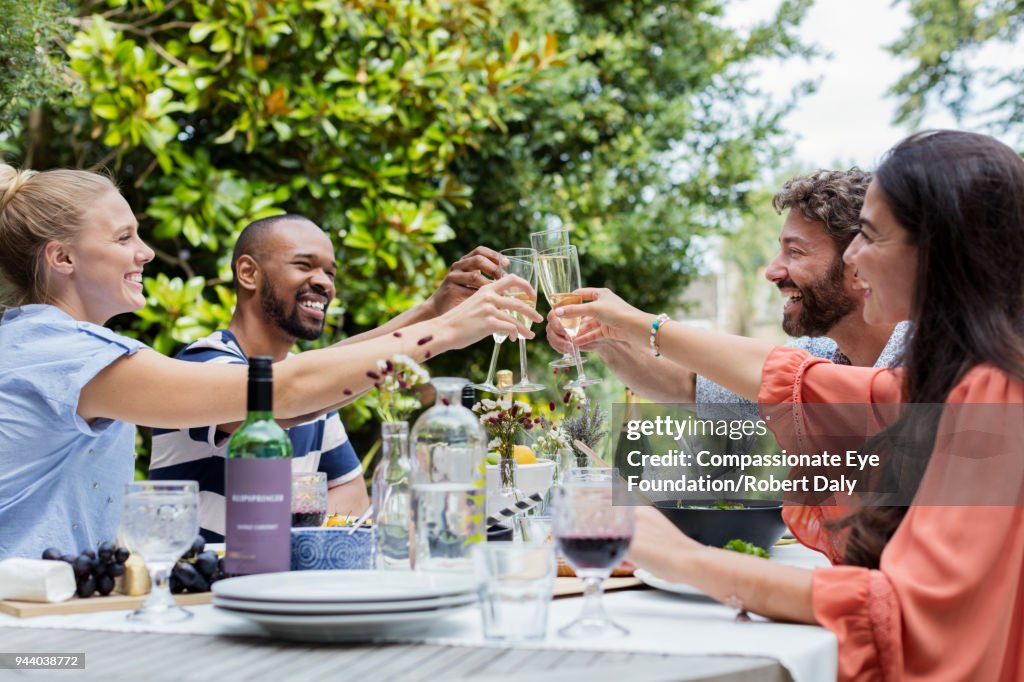 Smiling friends having lunch toasting with champagne glasses on garden patio