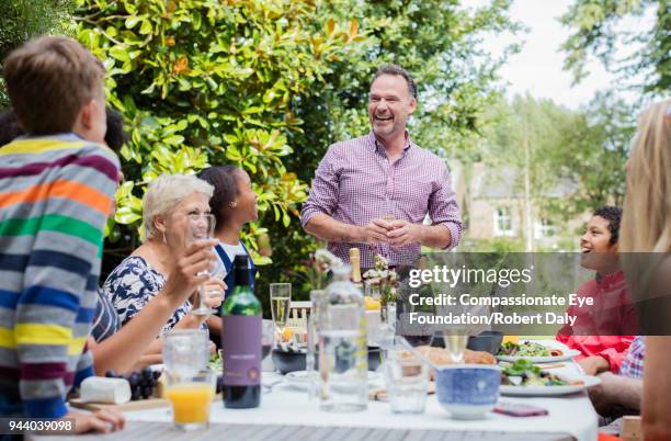 multi generation family enjoying lunch at garden patio table - moment friends men european stockfoto's en -beelden