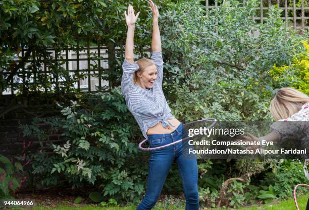 laughing playful woman spinning in plastic hoop in garden - gymnastikreifen stock-fotos und bilder