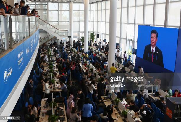 Journalists watch a screen showing a live image of China's President Xi Jinping as he delivers a speech during the opening of the Boao Forum for Asia...