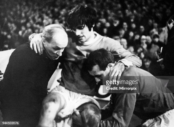Manchester United footballer George Best is helped off the pitch by trainer Jack Crompton and Ron Springett after becoming injured during the league...
