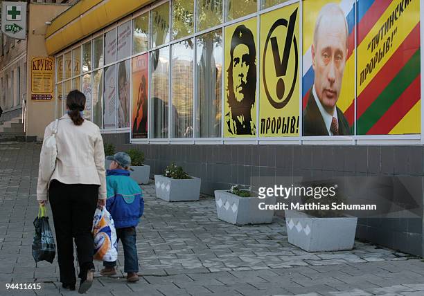 Mother and child pass a window of a youth organisation office with the faces of the former Russian president Vladimir Putin, the current president...