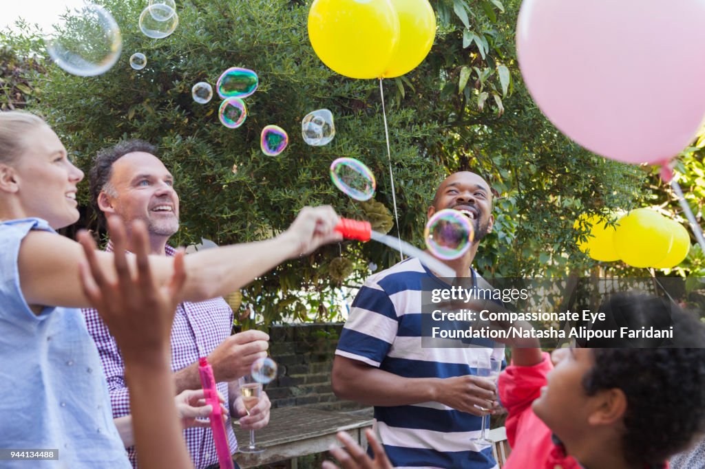 Multi generation family party on garden patio playing with bubbles and balloons