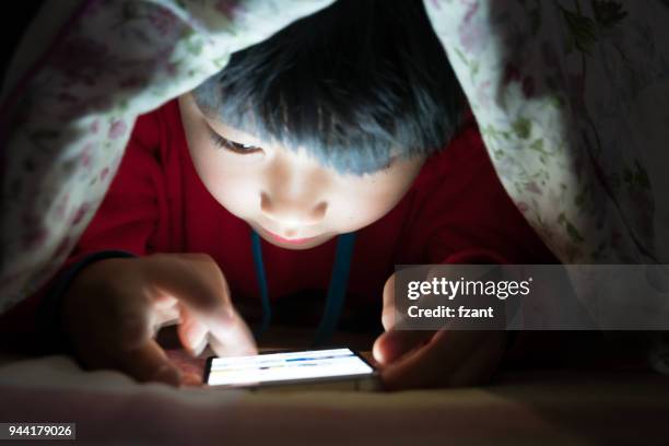 little boy on cell phone under duvet - child using a smartphone stock pictures, royalty-free photos & images