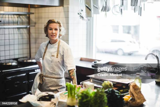 portrait of confident female owner standing by kitchen counter at restaurant - chef kitchen stockfoto's en -beelden
