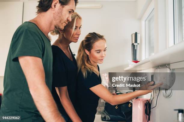 teenage girl pointing at equipment mounted on wall to parents at home - cable modems stock pictures, royalty-free photos & images