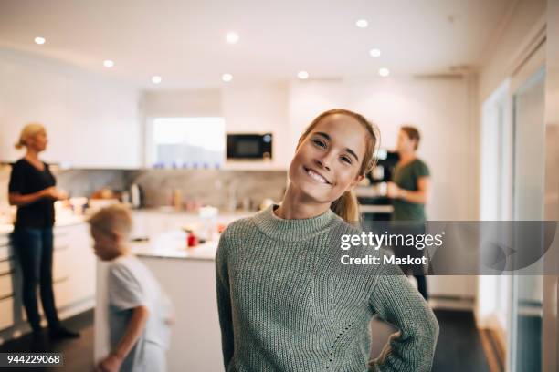 portrait of smiling teenage girl standing against family in kitchen - mutter tochter küche stock-fotos und bilder