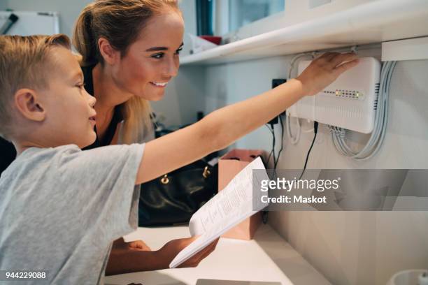 siblings adjusting household equipment with instruction manual at home - cable modems stock pictures, royalty-free photos & images