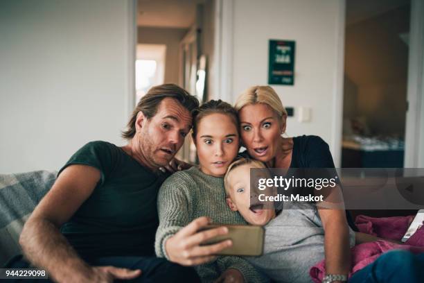 shocked family taking selfie through smart phone while sitting on sofa at home - sister stock photos et images de collection