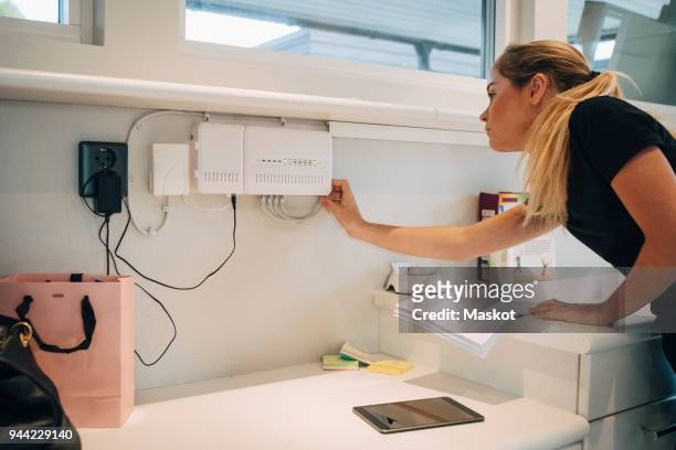 teenage girl adjusting cable of equipment mounted on wall at home - cable modems stock pictures, royalty-free photos & images