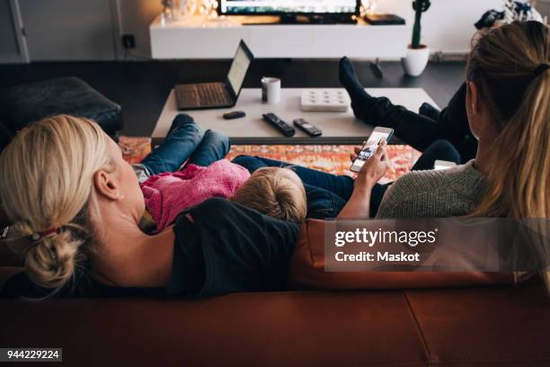 rear view of family sitting on sofa at home - men women & children film stock-fotos und bilder