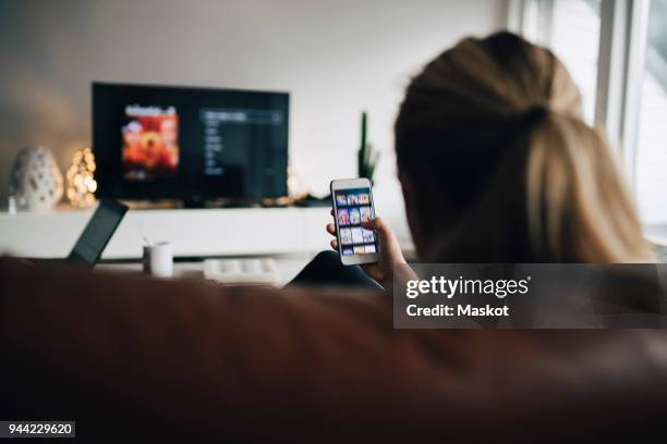 rear view of teenage girl using smart phone app while watching tv in living room at home - chica salon movil fotografías e imágenes de stock