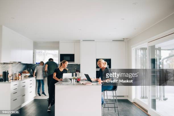 woman and teenage girl using laptops while man boy standing in kitchen at home - kitchen island stock pictures, royalty-free photos & images