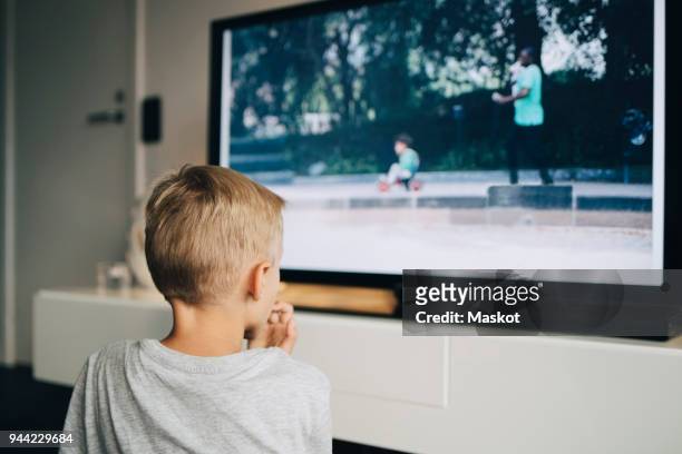 rear view of boy watching smart tv in living room at home - children watch tv stockfoto's en -beelden