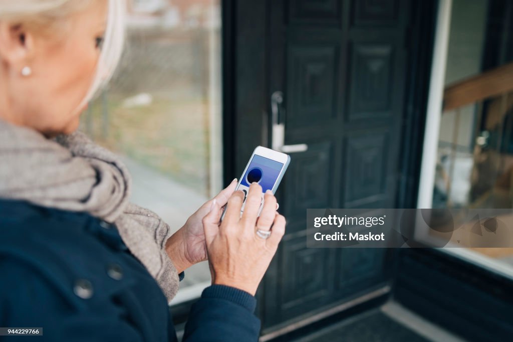 High angle view of woman unlocking house door through smart phone app
