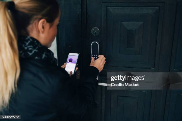 rear view of teenage girl using smart phone to unlock house door - serrure photos et images de collection