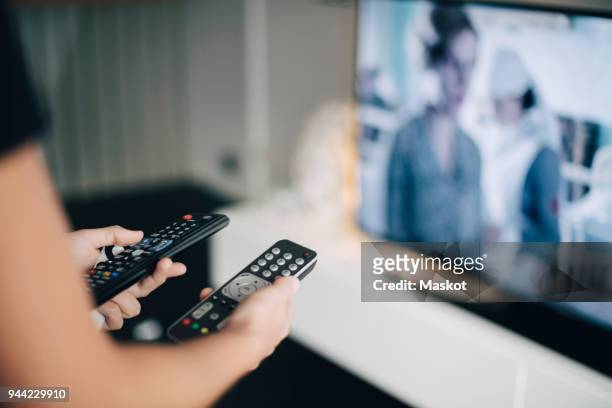 midsection of teenage girl holding remote controls by television set in living room at home - smart tv living room stock pictures, royalty-free photos & images