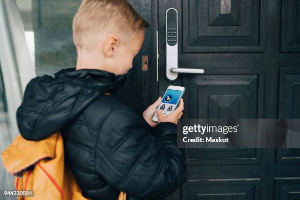 rear view of boy using app on smart phone to unlock house door - safe kids day stock pictures, royalty-free photos & images