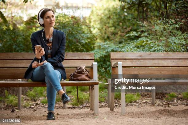 frau anhören von musik auf bank im park - park bench stock-fotos und bilder