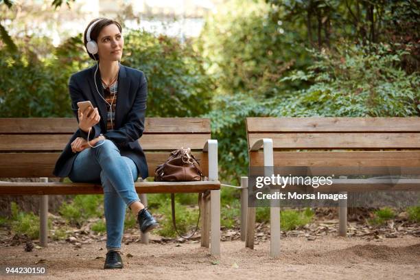 mujer escuchando música en el banco en el parque - banco del parque fotografías e imágenes de stock