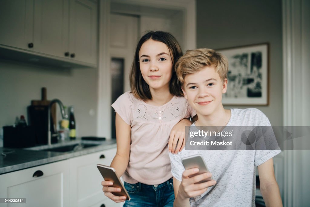 Portrait of smiling male and female friends holding smart phones at home