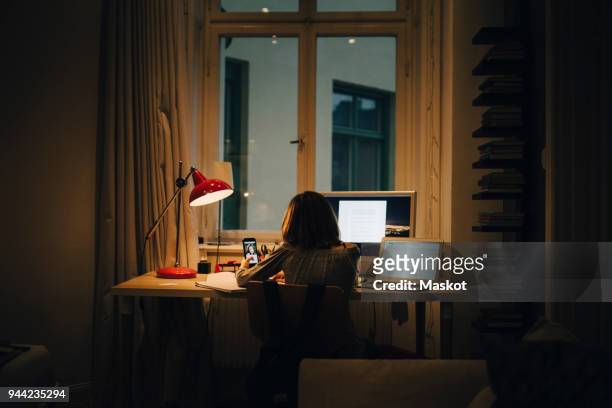 girl using laptop and computer while sitting at illuminated desk - desk lamp stockfoto's en -beelden