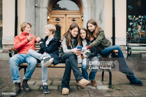 male and female friends talking while sitting on bench in city - small group of people stock-fotos und bilder