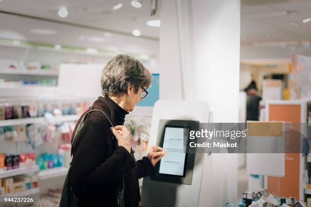 side view of senior woman using kiosk at pharmacy store - booth fotografías e imágenes de stock