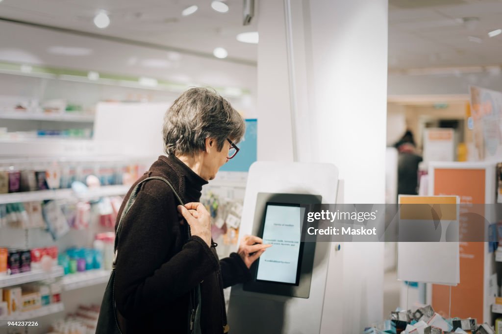 Side view of senior woman using kiosk at pharmacy store