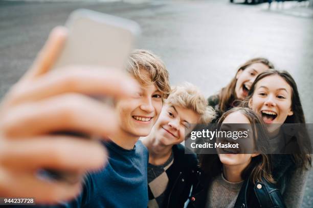 smiling male taking selfie with friends through smart phone while standing in city - adolescence stock pictures, royalty-free photos & images