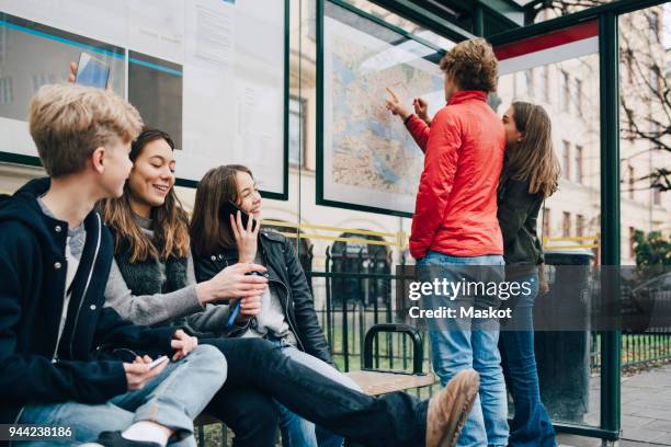 male and female friends waiting at bus stop in city - bus bench stock-fotos und bilder