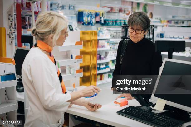female owner holding prescription paper with senior customer standing at checkout in pharmacy store - apotheek stockfoto's en -beelden