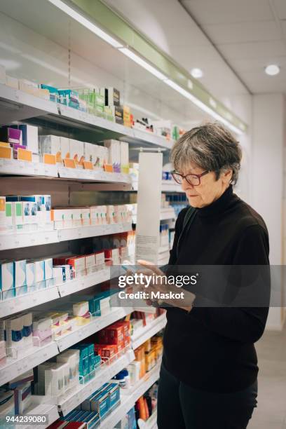 senior female customer examining medicine by rack at pharmacy store - tool rack ストックフォトと画像