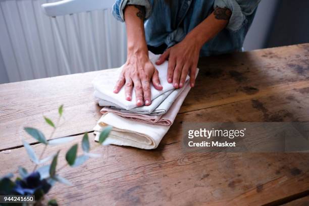 midsection of woman folding napkins while standing at wooden table in kitchen - napkin stock pictures, royalty-free photos & images