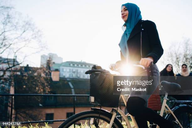 Back lit of young woman cycling by female friends against sky in city