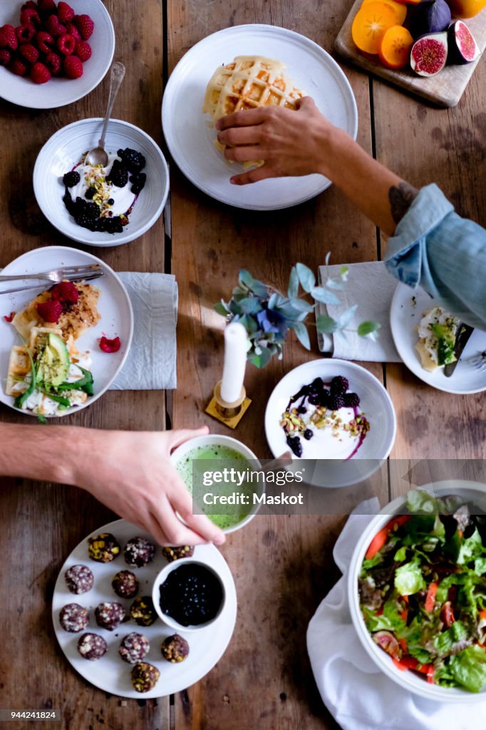 Cropped hands of couple having food at table while sitting by wall