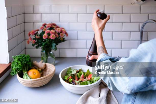 cropped image of woman seasoning salad at kitchen counter - pepper mill stockfoto's en -beelden