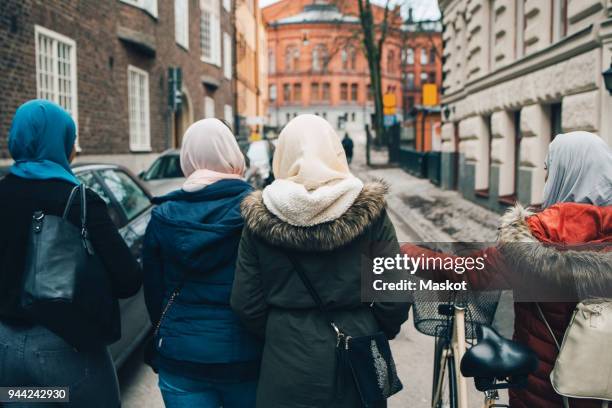 rear view of female friends walking with bicycle on street in city - hijab woman from behind stock-fotos und bilder