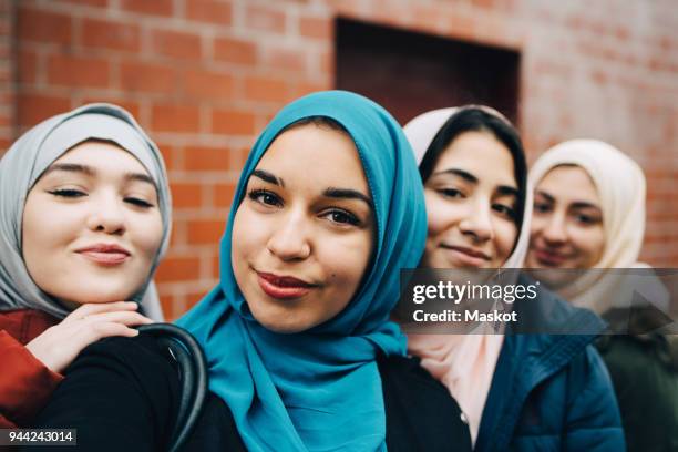 portrait of smiling muslim friends against building in city - hijab girl ストックフォトと画像