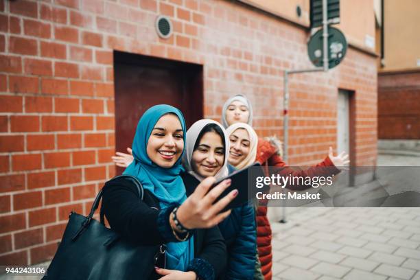 happy woman taking selfie with female friends on sidewalk against building in city - young muslim stockfoto's en -beelden