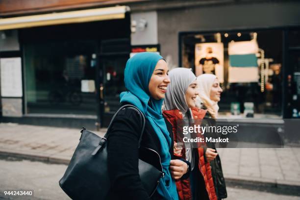 Cheerful young female friends walking with arms in arms on street in city