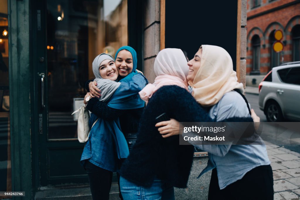 Smiling multi-ethnic female friends greeting on sidewalk in city