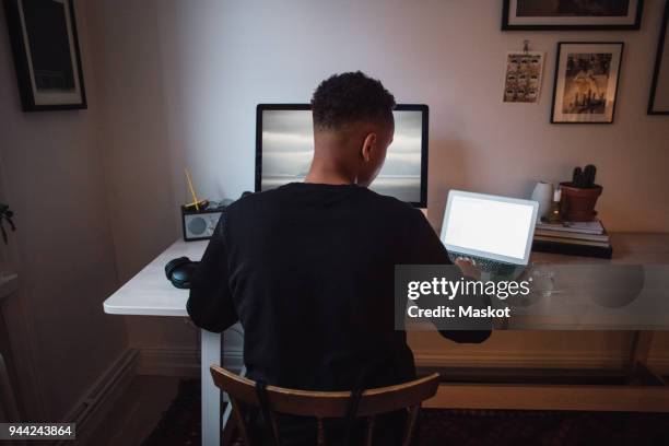 rear view of young freelance worker using laptop and computer at desk - computer monitor back stock pictures, royalty-free photos & images