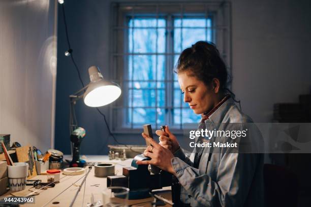 female engineer working on equipment at illuminated desk by window in workshop - schreibtischlampe stock-fotos und bilder