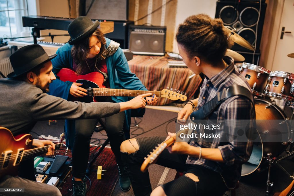 Man teaching female friend while playing guitar at recording studio during rehearsals