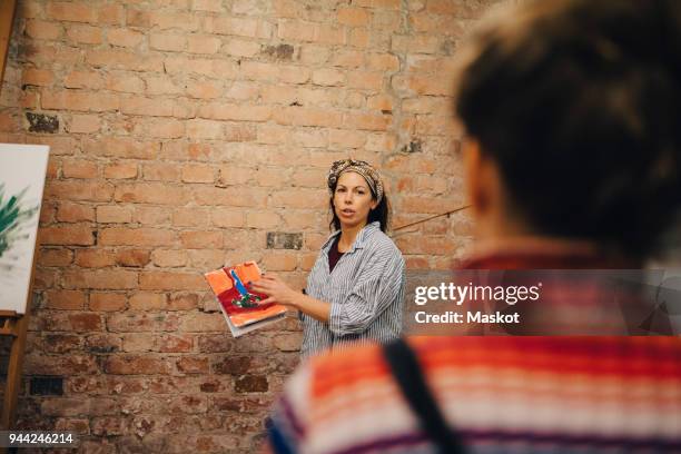 instructor showing painting to artist while standing against brick wall at studio - kunstatelier stockfoto's en -beelden