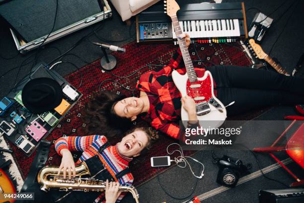 high angle view of happy female musicians playing instruments while lying on carpet - artiste musique photos et images de collection