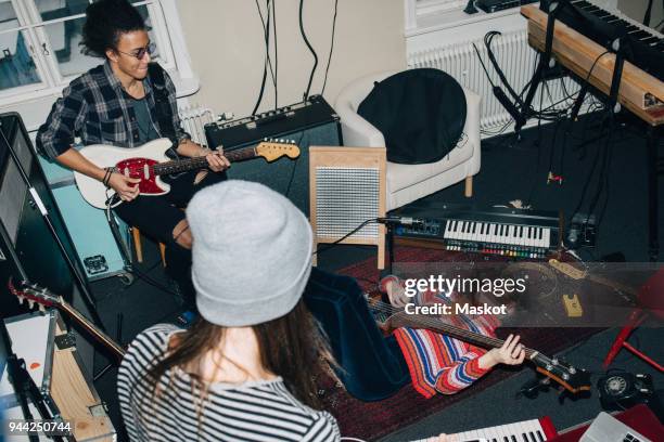 high angle view of male and female friends playing guitars while rehearsing in studio - bandprobe stock-fotos und bilder