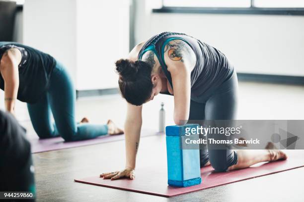 Woman with one arm in cat pose during hot yoga class in fitness studio