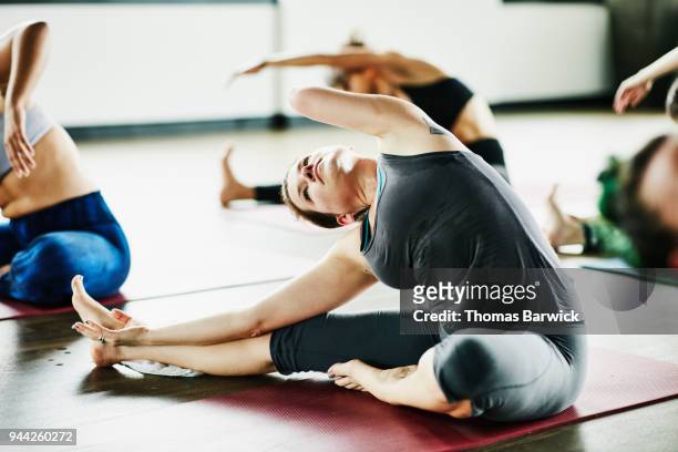 Woman with one arm in seated side bend pose during hot yoga class